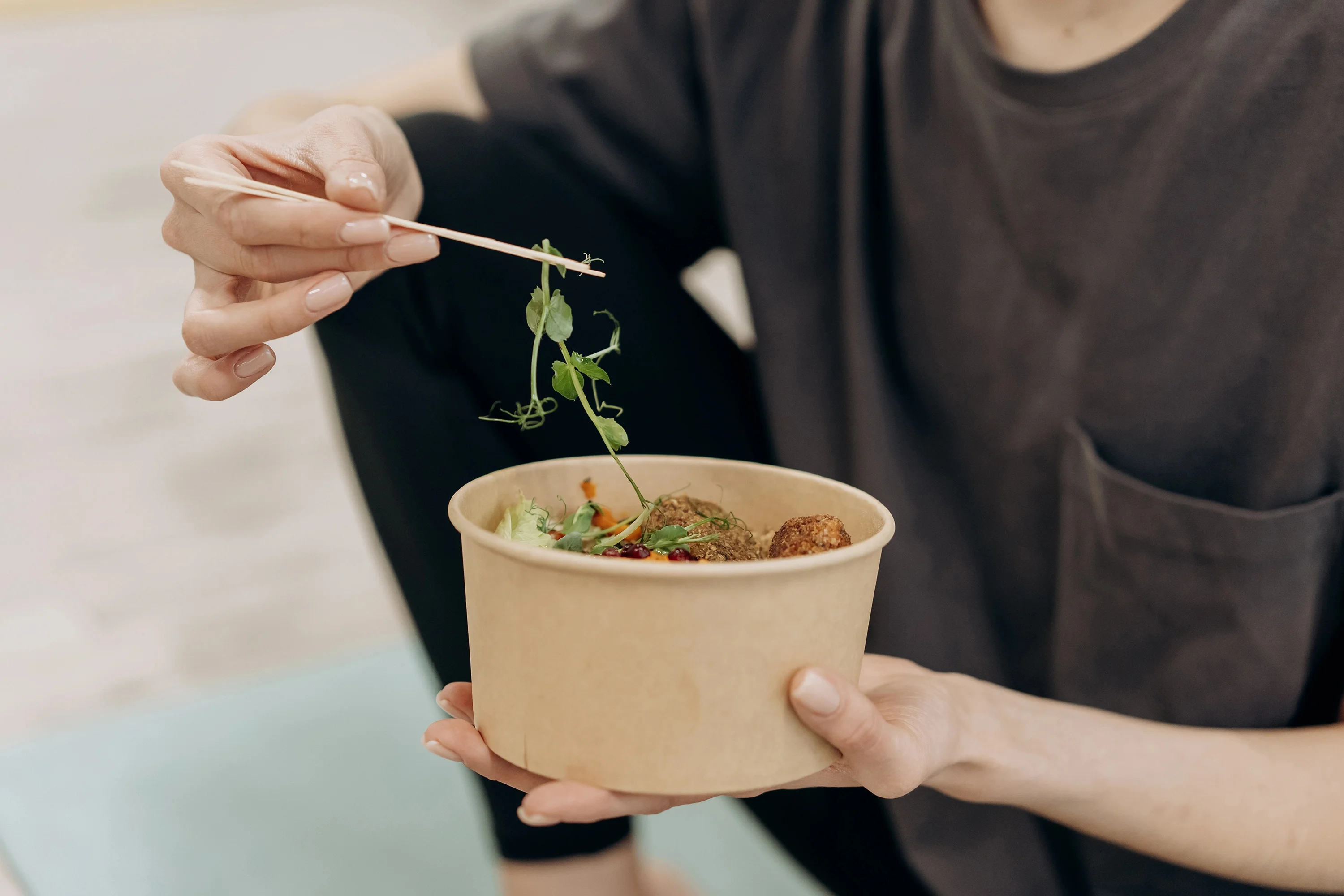 person eating veggies out of a bowl with chop sticks